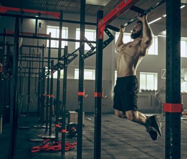 Concept: power, strength, healthy lifestyle, sport. Powerful attractive muscular man trainer do pull ups during workout at the gym